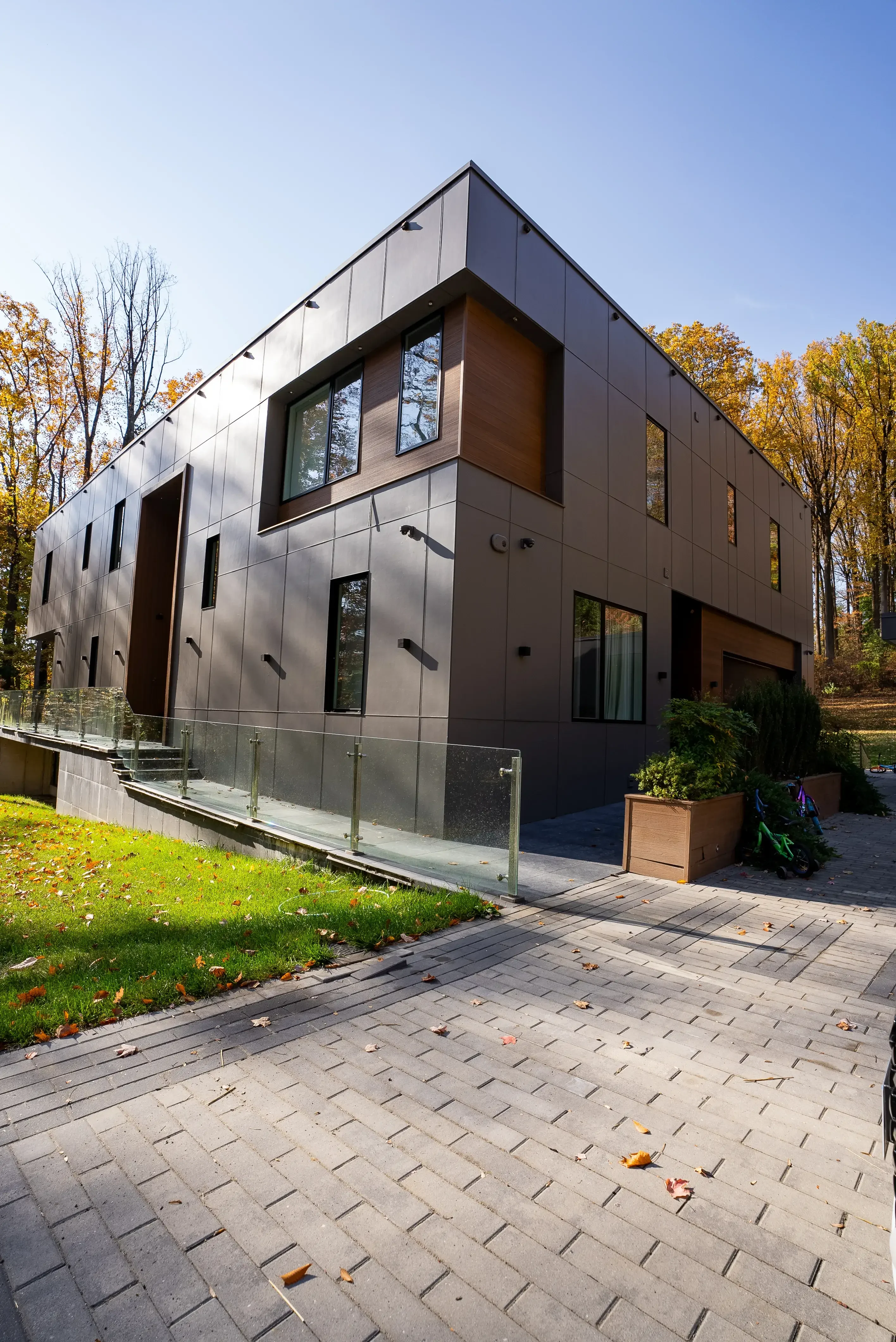 Modern home with sleek black exterior, large windows, and glass railing, surrounded by a landscaped yard and trees.