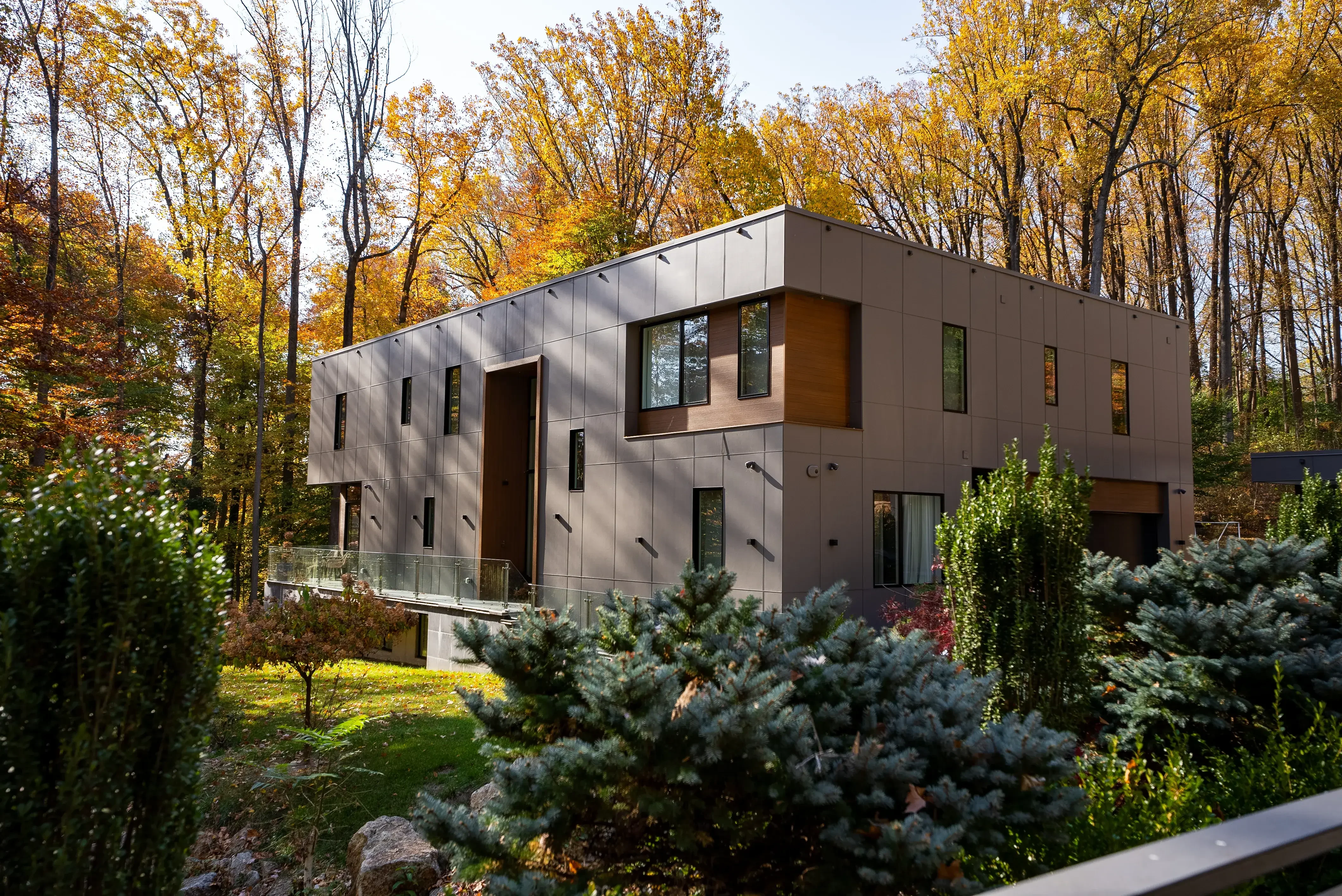 A modern house with clean lines and large windows, surrounded by vibrant autumn trees and greenery in the foreground.