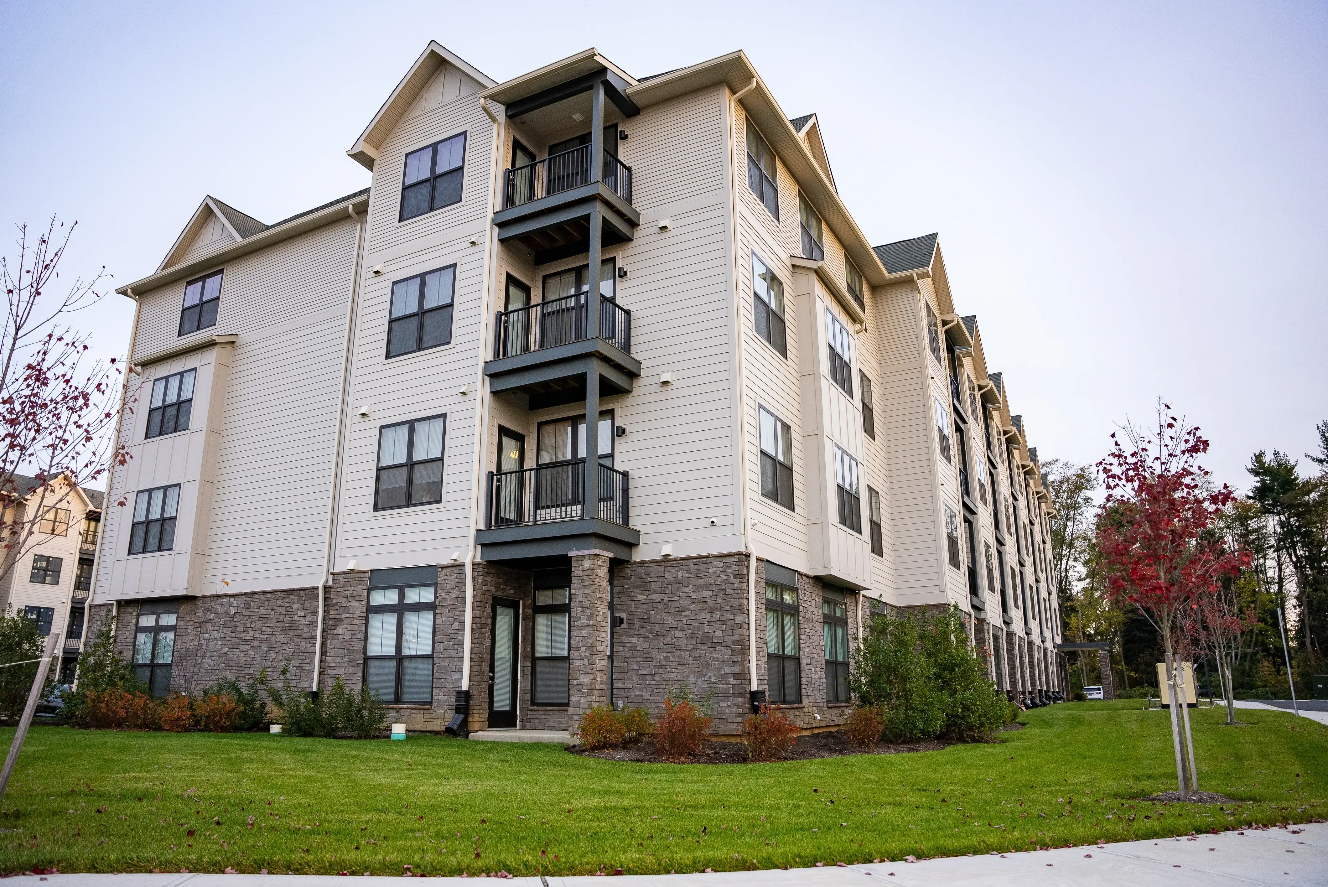 This image highlights a section of a completed multi-family building, showcasing its modern design with a combination of siding, stonework, and private balconies. It emphasizes the quality and attention to detail in the construction.