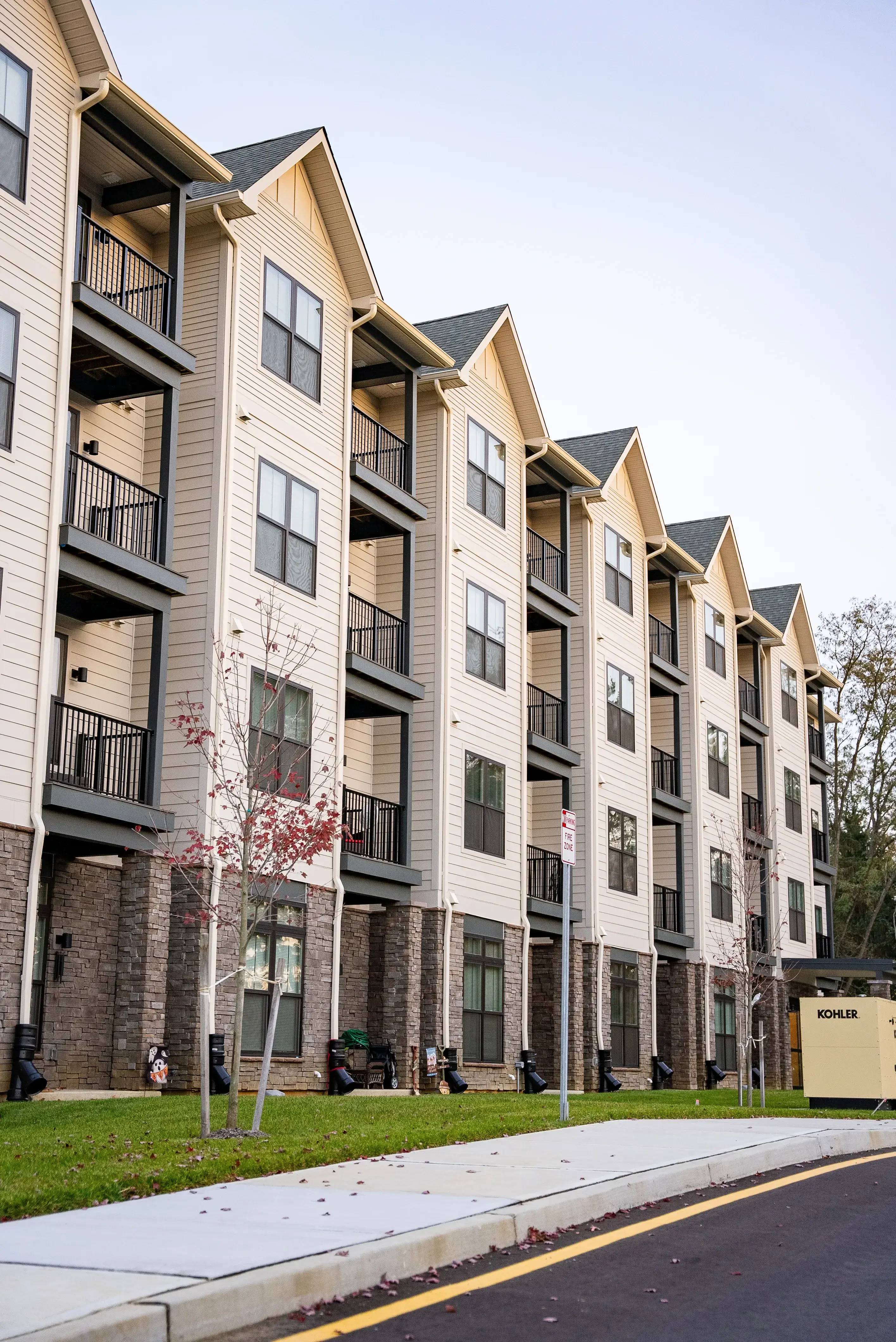 A row of modern apartment buildings with balconies, stone accents, and well-maintained surroundings, viewed from the street.