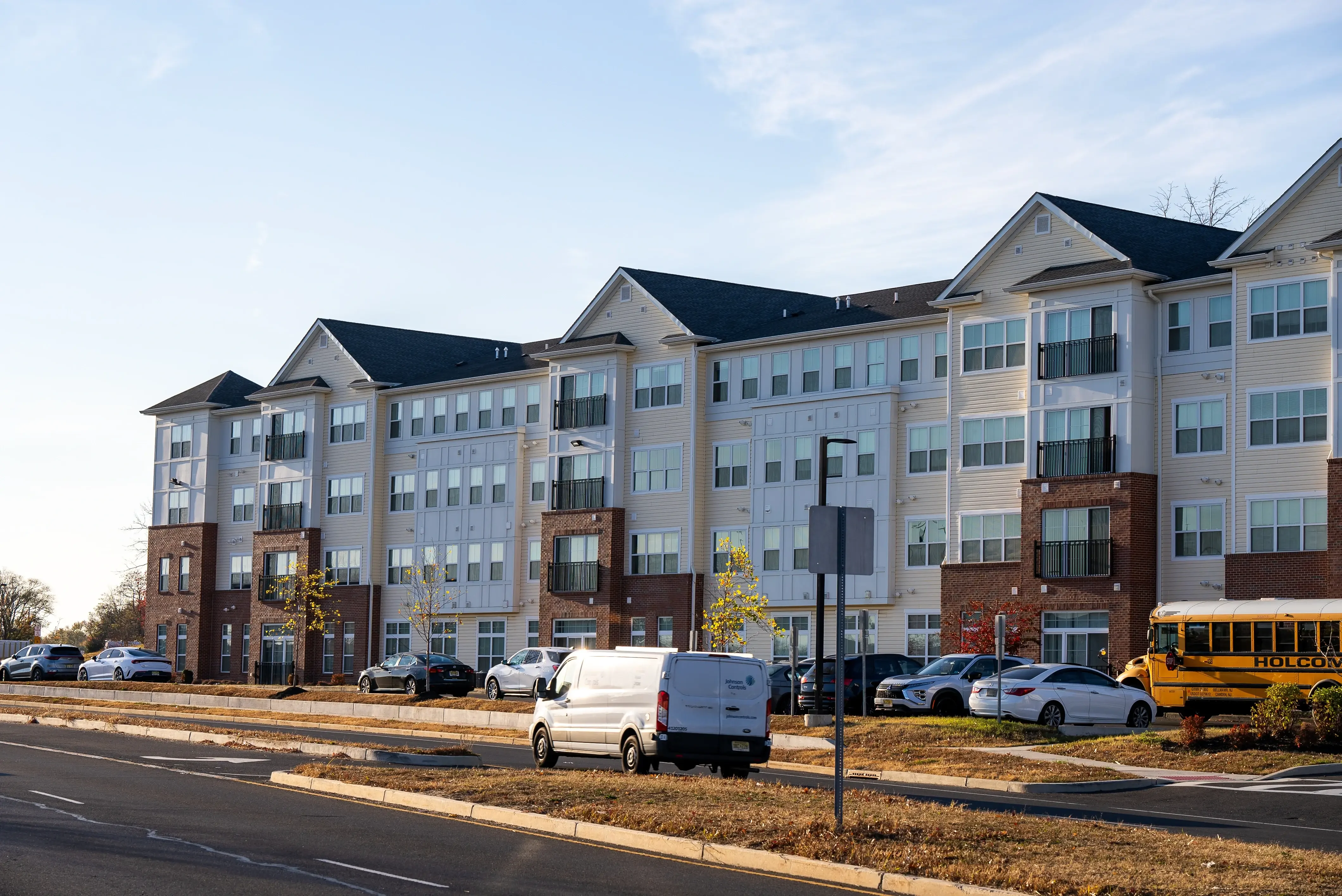 This image captures a modern multi-family residential building, combining clean lines and materials such as brick and siding for a balanced aesthetic. The large windows offer abundant natural light, while balconies provide outdoor spaces for residents. Ample parking and the presence of vehicles suggest a well-utilized urban community. Let me know if you'd like any analysis or information highlighted further!