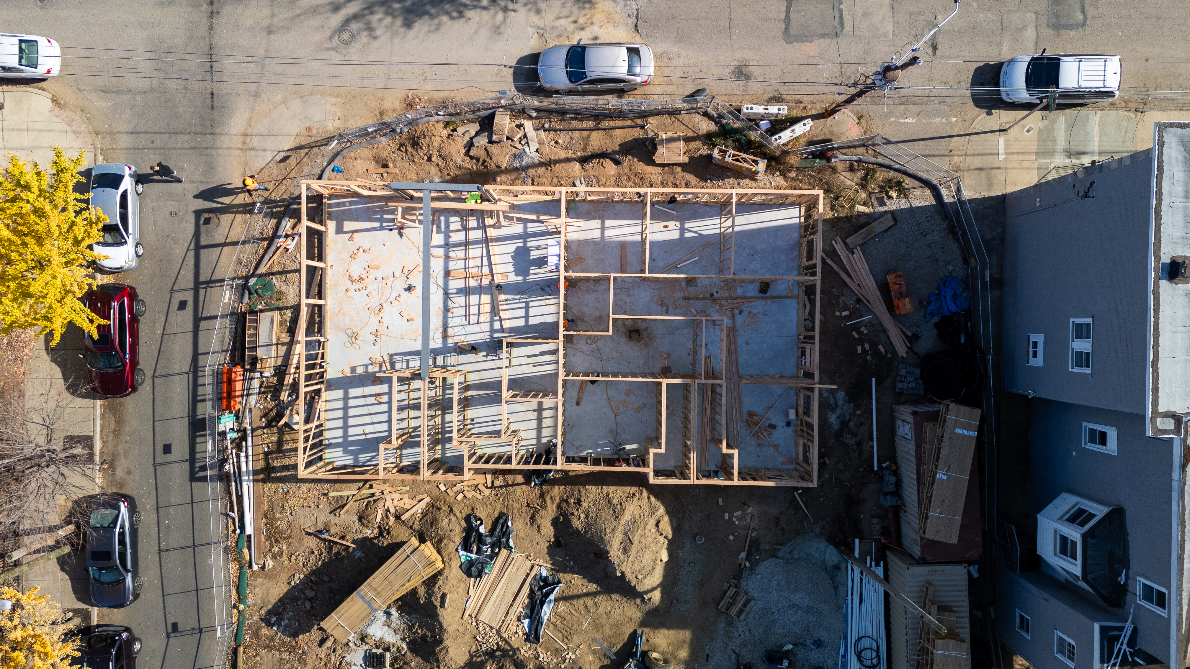 This aerial image captures the construction of a building foundation and wooden framing, surrounded by construction materials, vehicles, and workers.